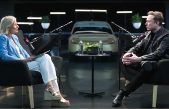 Elon Musk interviewé par une femme, voiture électrique en fond.