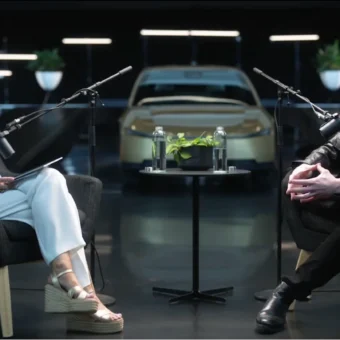 Elon Musk interviewé par une femme, voiture électrique en fond.