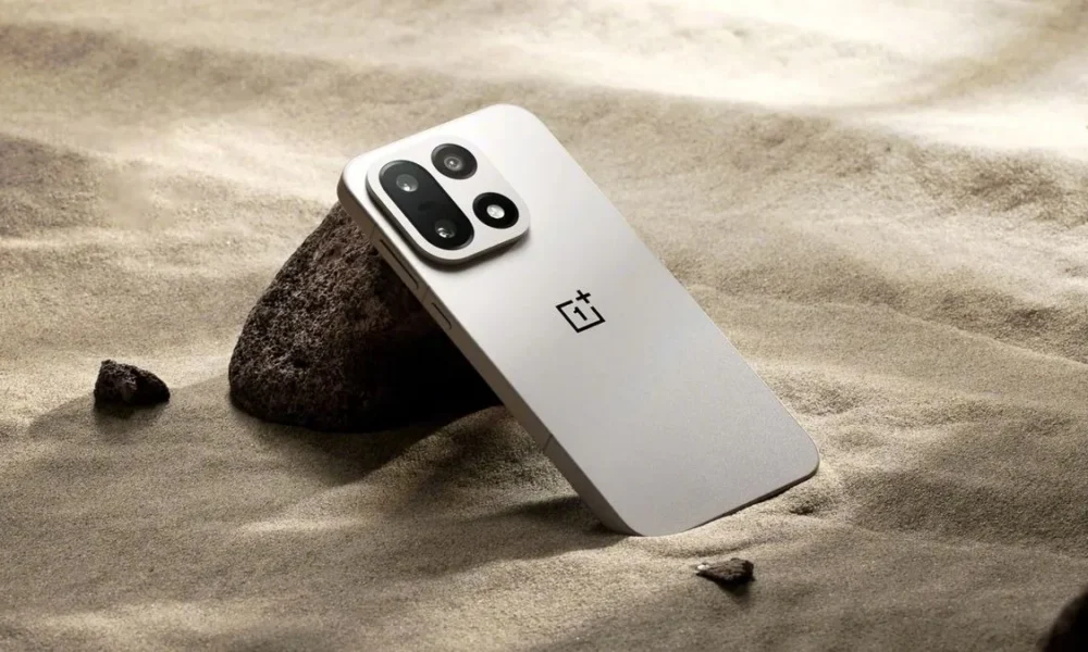 Smartphone OnePlus gris clair sur sable avec rochers.