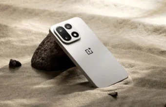 Smartphone OnePlus gris clair sur sable avec rochers.