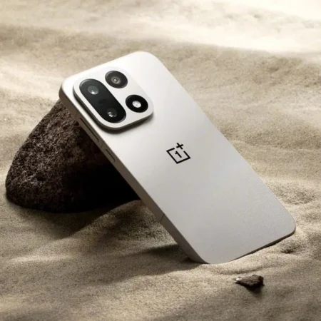 Smartphone OnePlus gris clair sur sable avec rochers.