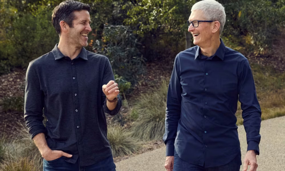 Deux hommes souriants, dont Tim Cook, marchant ensemble en extérieur.