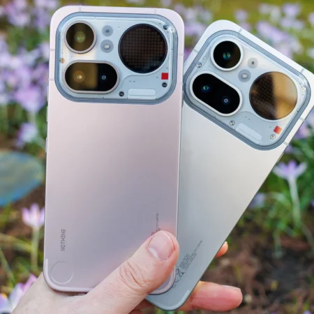 Deux Nothing Phone (2a) rose et blanc tenus près de fleurs.