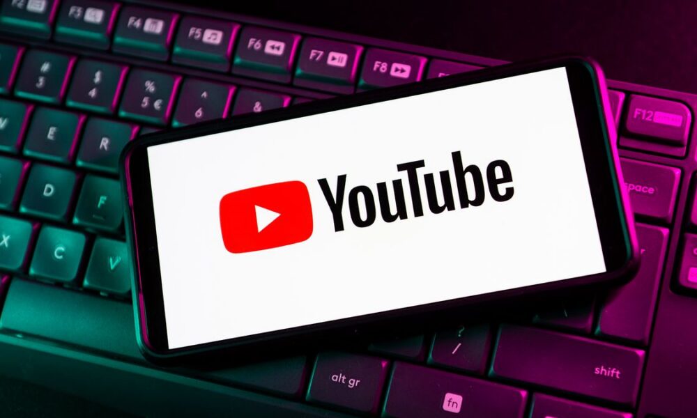 Logo YouTube sur smartphone posé sur clavier d'ordinateur rétroéclairé.